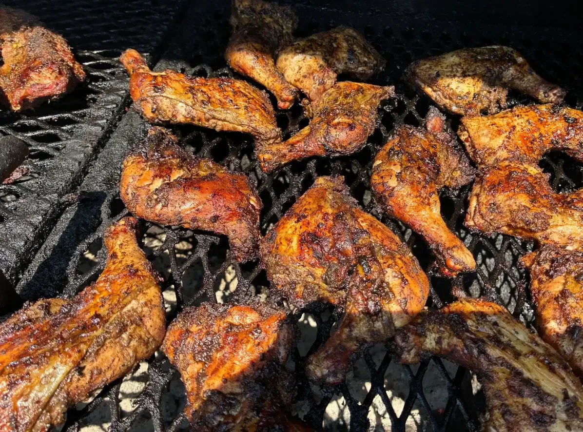 Jerk chicken quarters and rib tips searing over open charcoal at HoneyBee's Kitchen in Grand Rapids